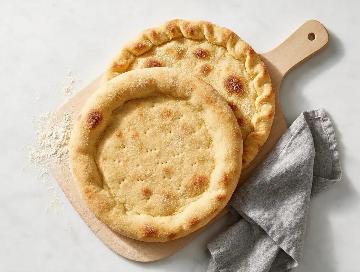 Par-baked round foxtail millet pizza base with a raised rim on a wooden board